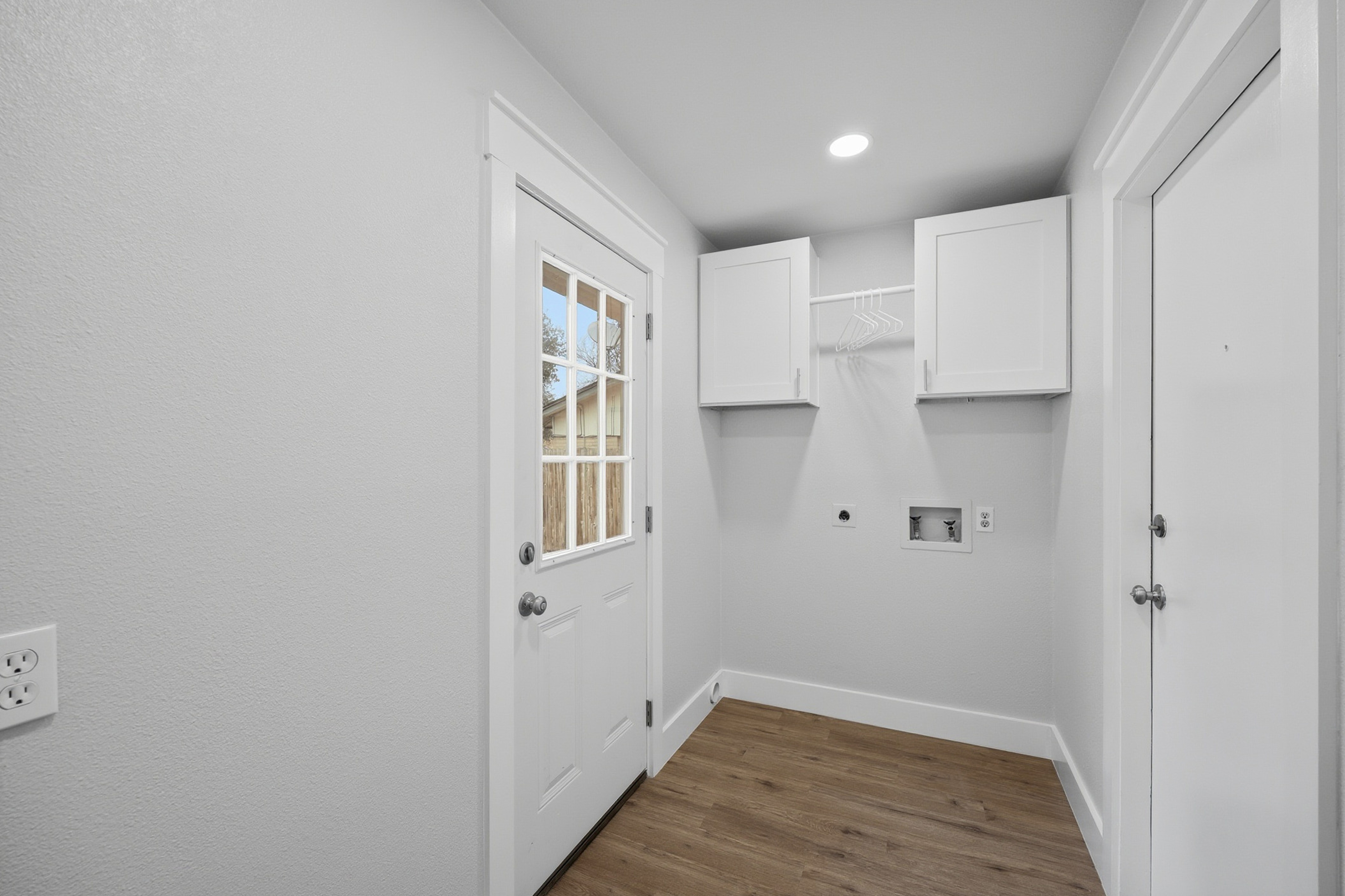 Dedicated laundry room with white upper cabinets, backyard door, and utility hookups
